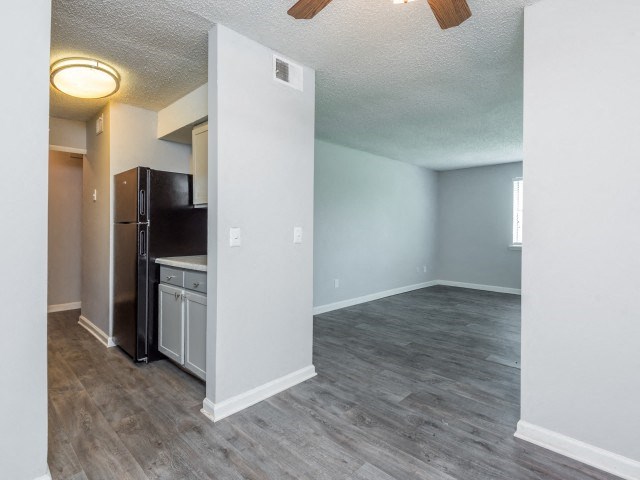 an empty living room with a kitchen and a ceiling fan