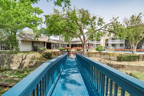 a blue bridge over a swimming pool with houses in the background