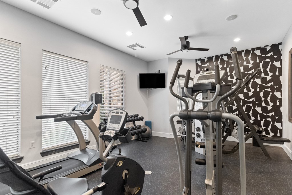 a gym with cardio machines and a tv