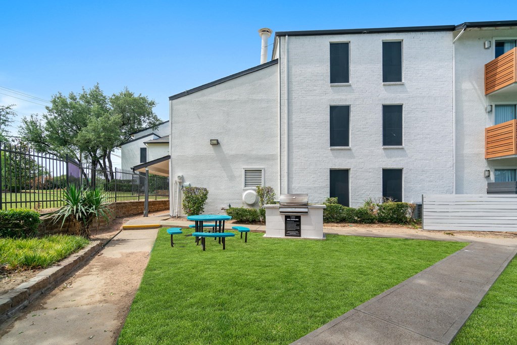 a patio with a grill and picnic table in front of a white building