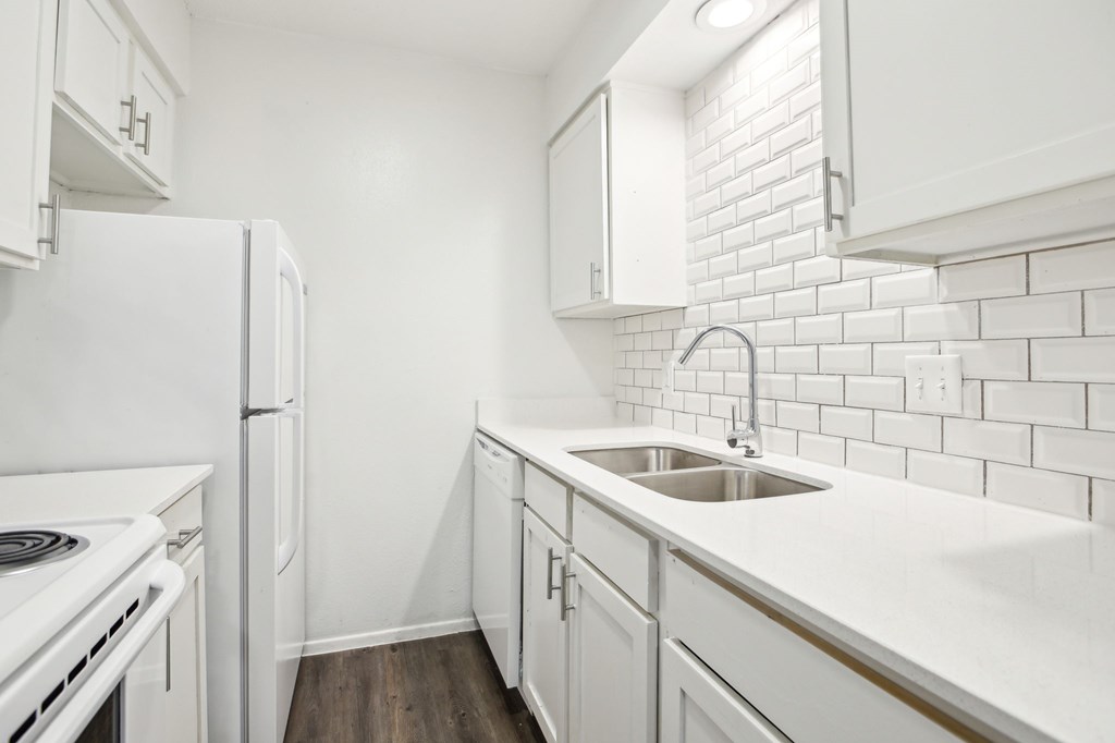 A white kitchen with a white fridge and white cabinets.
