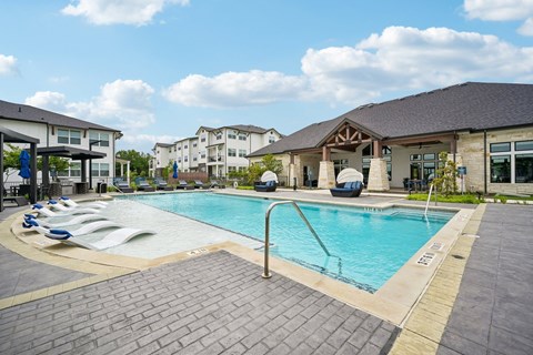 A large outdoor swimming pool surrounded by a brick patio and lounge chairs.
