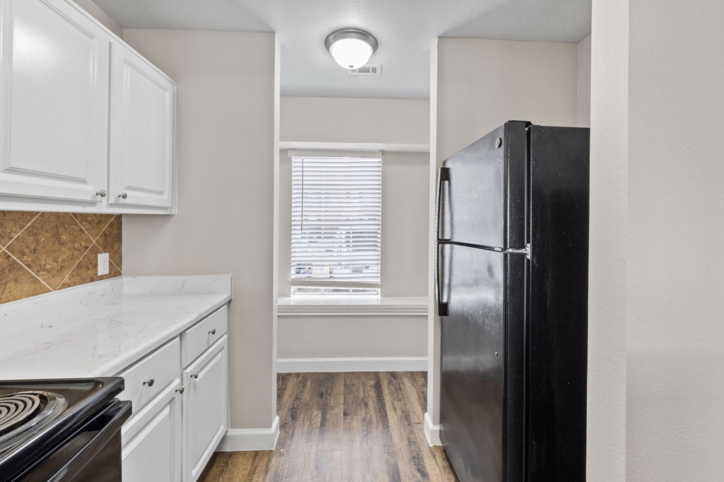 A kitchen with a black fridge, white cabinets and a stove top.