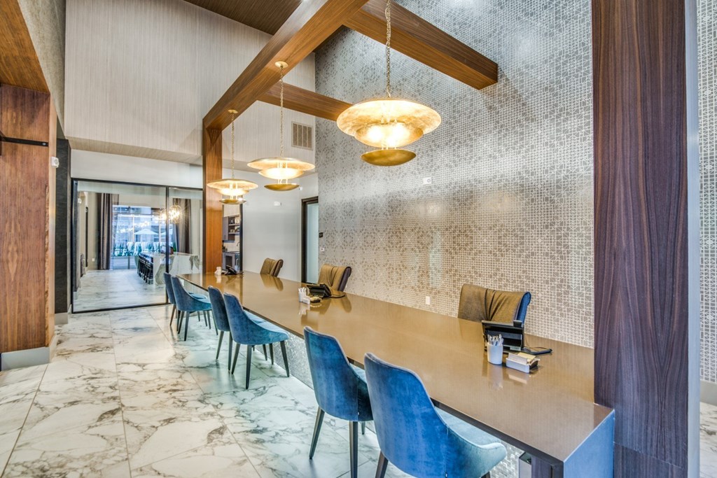 A long wooden table with blue chairs is in the foreground of a marble floor.