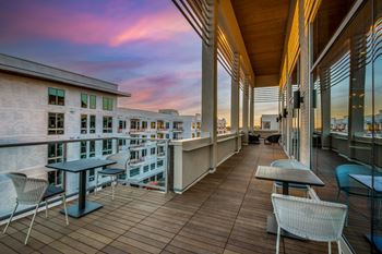A balcony with chairs and tables overlooks a cityscape at dusk.