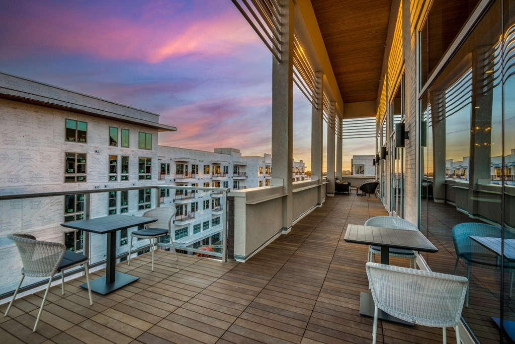 A balcony with a table and chairs overlooks a cityscape at dusk.