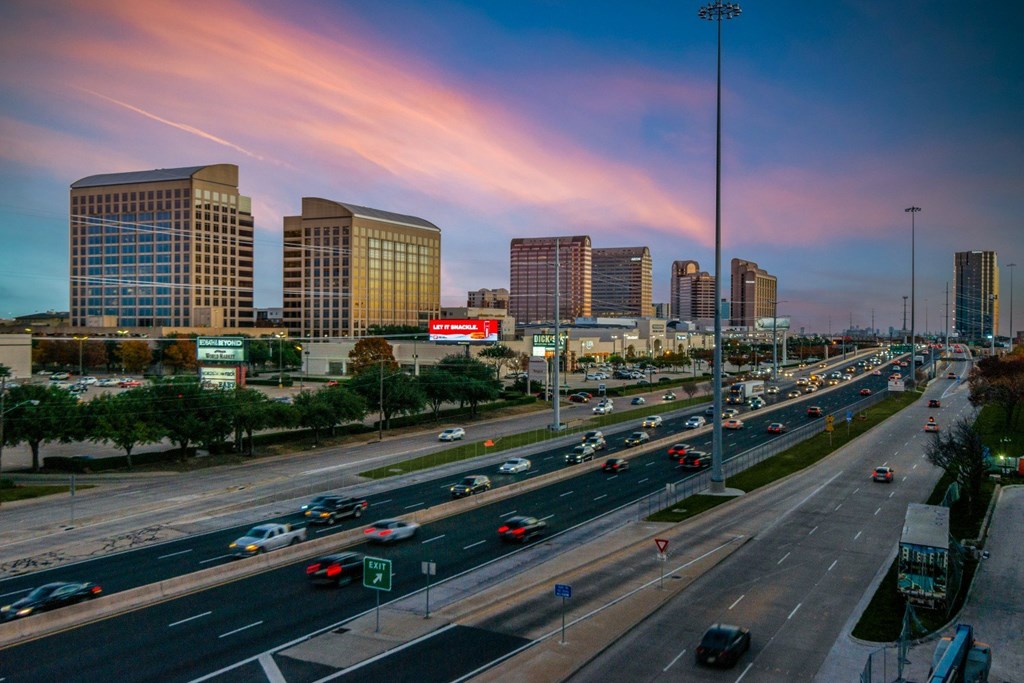 A busy highway with cars driving in both directions and tall buildings in the background.