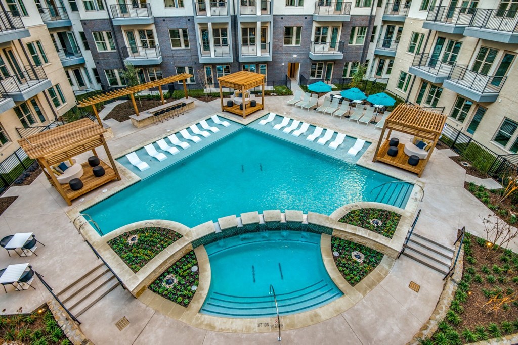 A large outdoor swimming pool surrounded by a patio area with chairs and umbrellas.