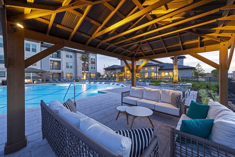 a swimming pool with lounge chairs and tables under a wooden roof
