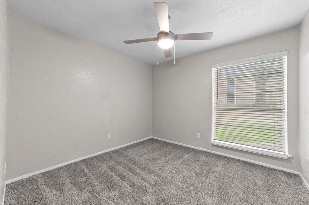 an empty bedroom with a ceiling fan and a window
