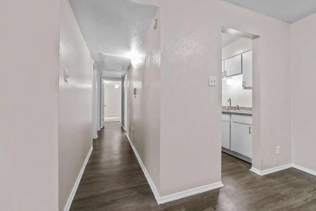 a long hallway with white walls and a kitchen in the distance