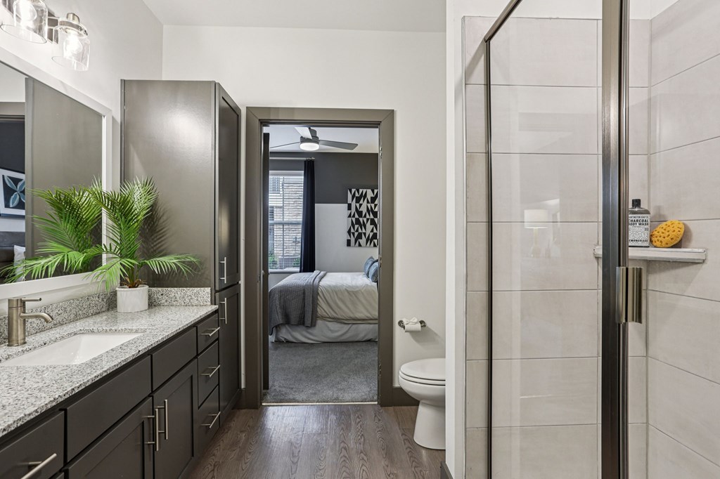 A bathroom with a walk-in shower and a bedroom in the background.