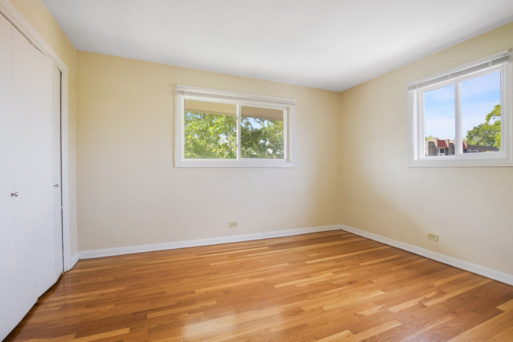 an empty room with wooden floors and two windows