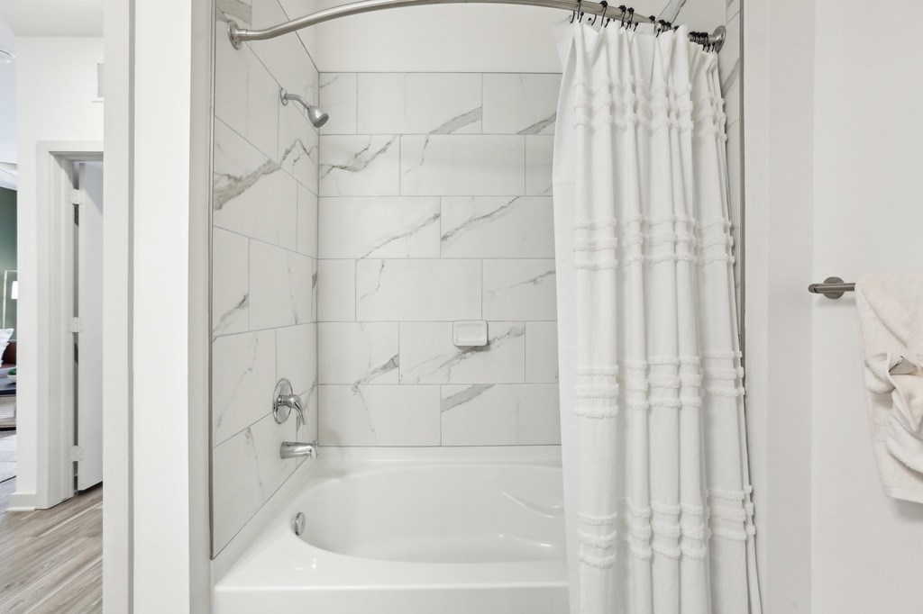 A white bathroom with a marble tile wall and a white tub.
