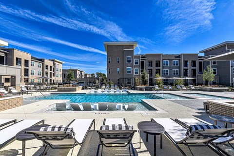 A large swimming pool surrounded by lounge chairs and buildings in the background.