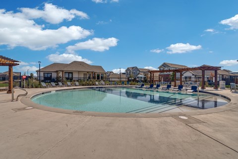 A large outdoor swimming pool surrounded by a fence and a pergola.