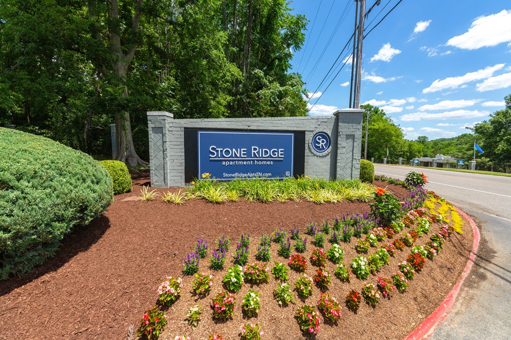 a stone ridge sign with flowers and bushes in front of it
