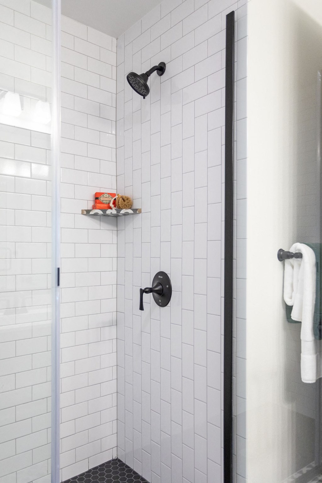 a white tiled shower with a glass door and a black shower head
