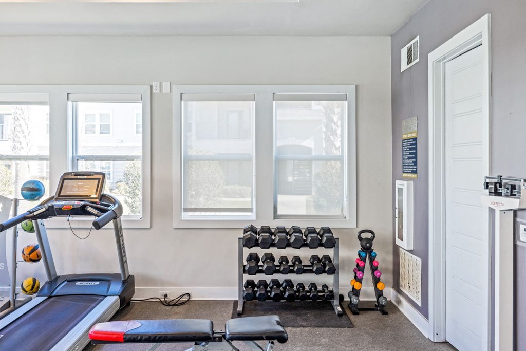 A room with a treadmill, dumbbells, and a bench.
