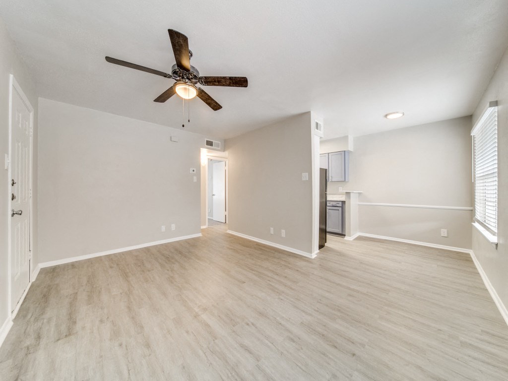 an empty living room with a ceiling fan and a kitchen