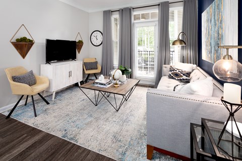 A living room with a grey sofa, a wooden chair, a white cabinet, a TV, a clock, and a rug.