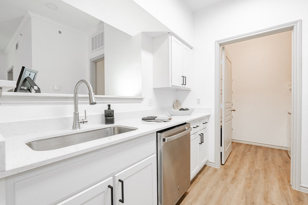 a kitchen with white cabinets and a sink and a door to a hallway