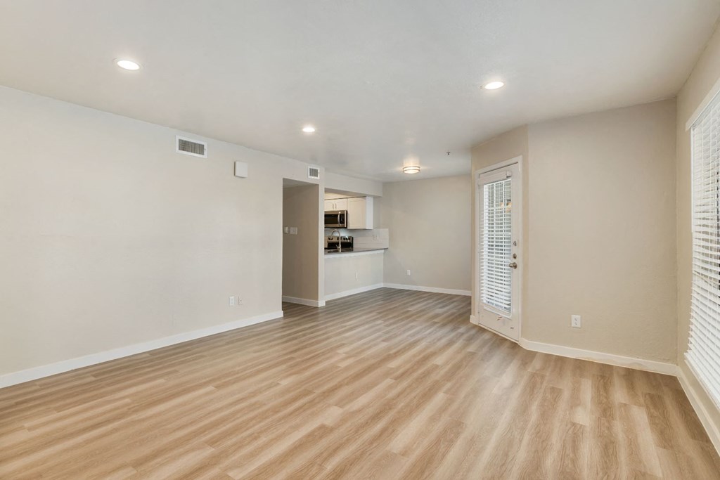 an empty living room with a kitchen in the background