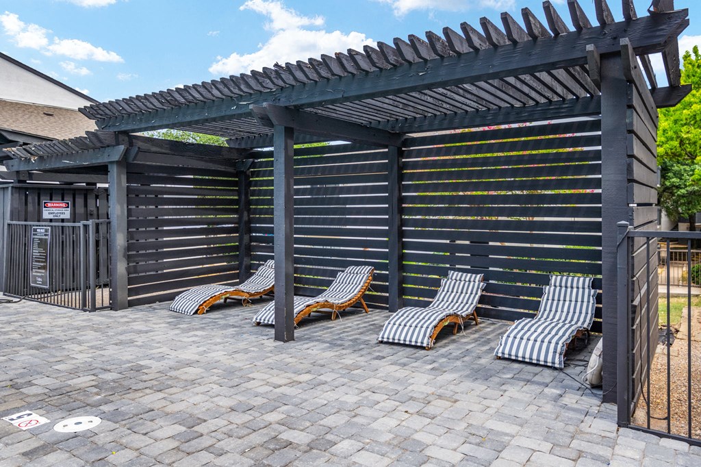 a pergola with chaise lounges on a brick patio