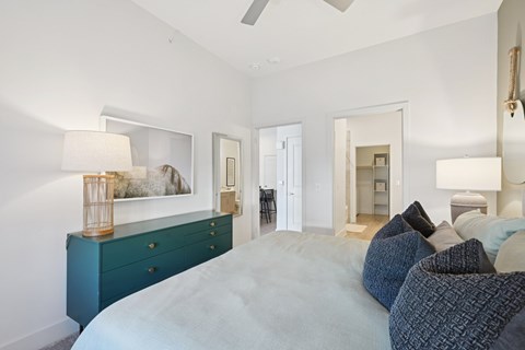 A bedroom with a large bed and a dresser with a lamp on top.