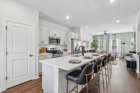 A modern kitchen with white cabinets and a long island with chairs.