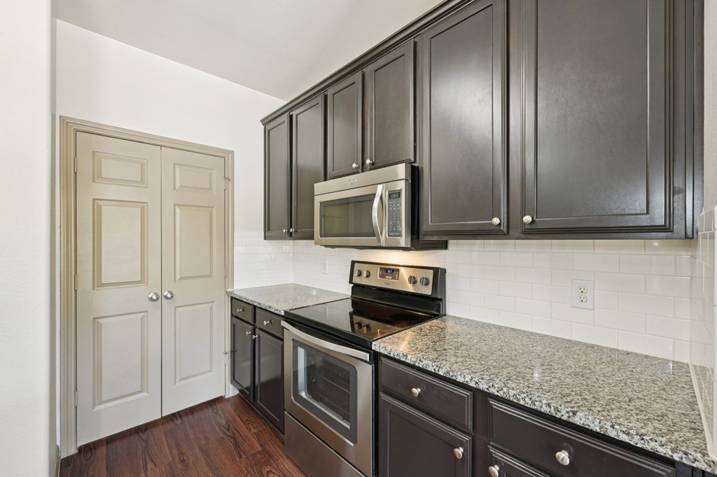 A kitchen with dark brown cabinets and a granite countertop.