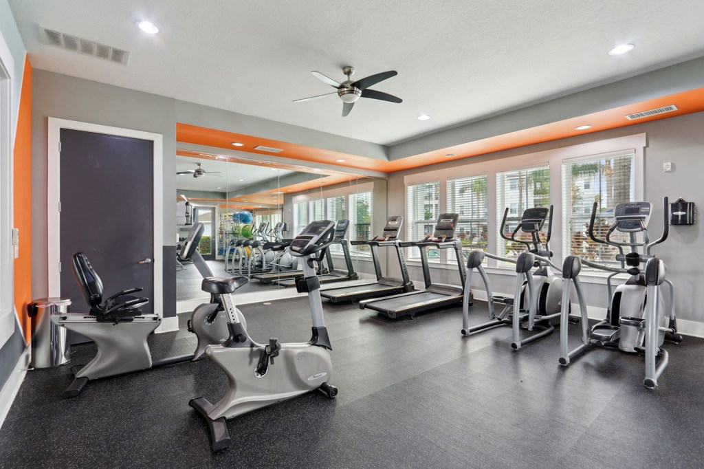 A gym with a variety of equipment including treadmills, stationary bikes, and elliptical machines.