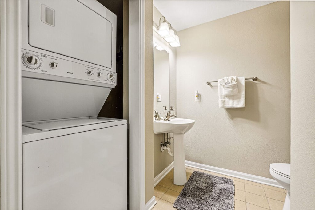 A white washing machine is in a bathroom next to a white sink.