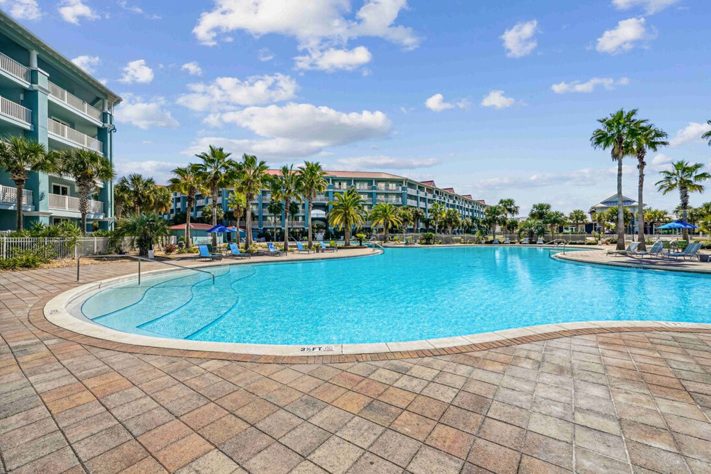 A large swimming pool surrounded by a brick patio and palm trees.