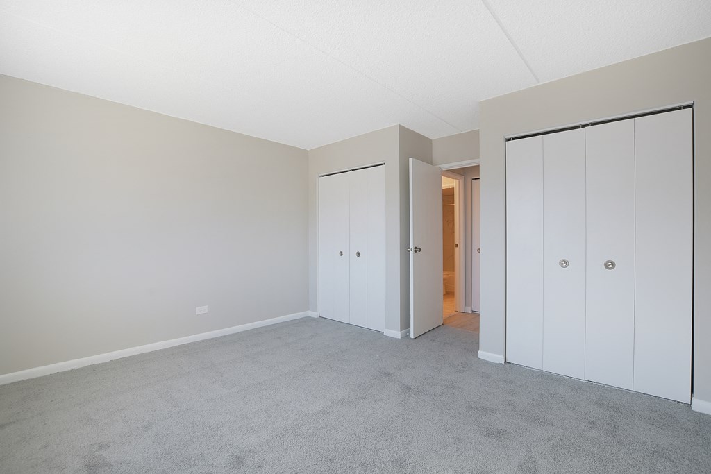 an empty bedroom with white closets and a carpeted floor
