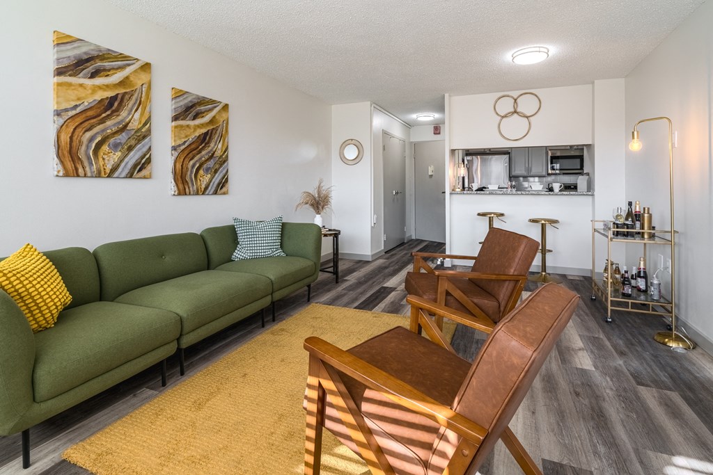 a living room with a green couch and two chairs and a kitchen in the background