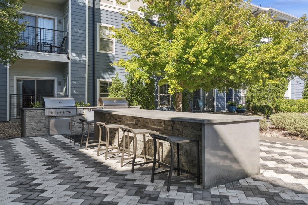 A patio with a bar and chairs is surrounded by a building and trees.