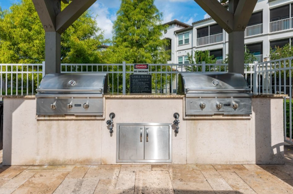 two stainless steel bbq grills on a concrete wall with a sign in the background