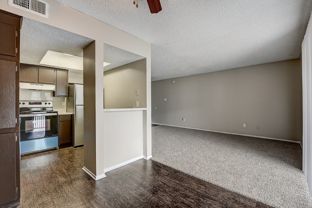 an empty living room with a kitchen in the background