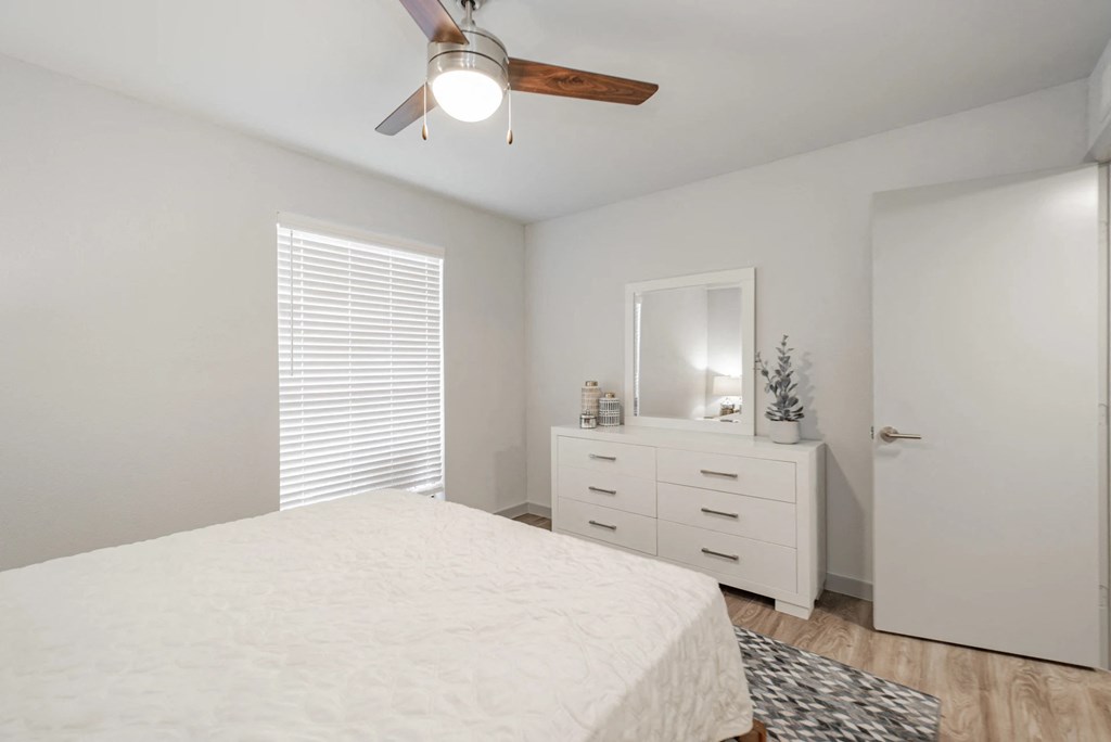 A white bedroom with a bed, dresser, mirror, and a ceiling fan.