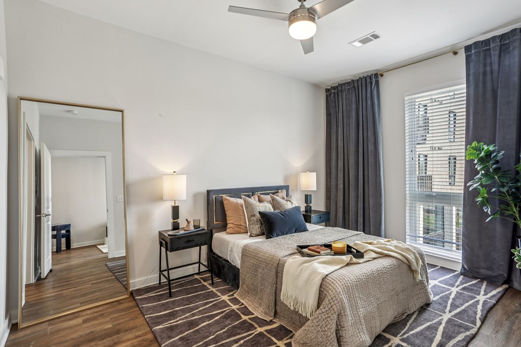 A bedroom with a large bed, a ceiling fan, and a view of a building outside the window.