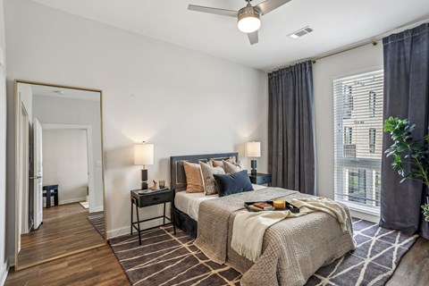A bedroom with a large bed, a ceiling fan, and a view of a building outside the window.