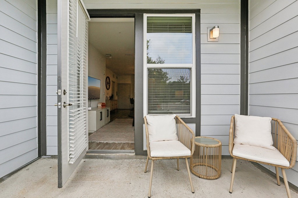 Two chairs and a table are on a porch.
