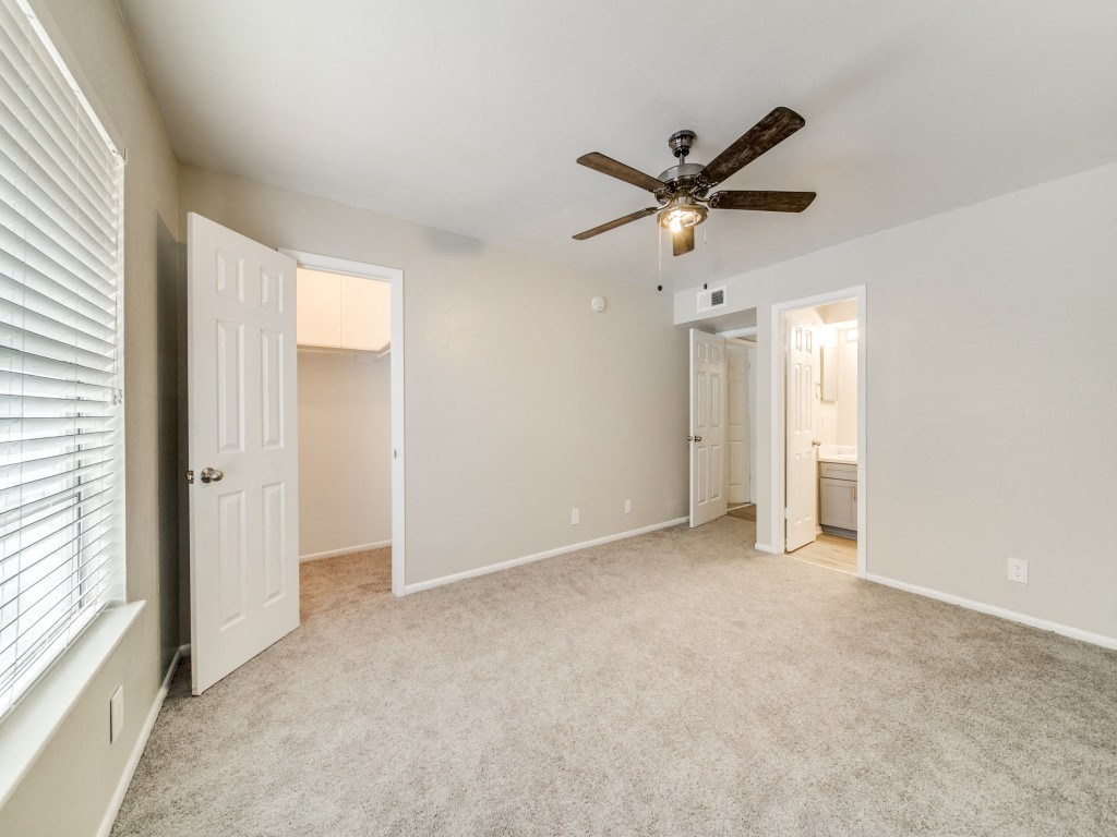 an empty living room with a ceiling fan and a door to a bathroom