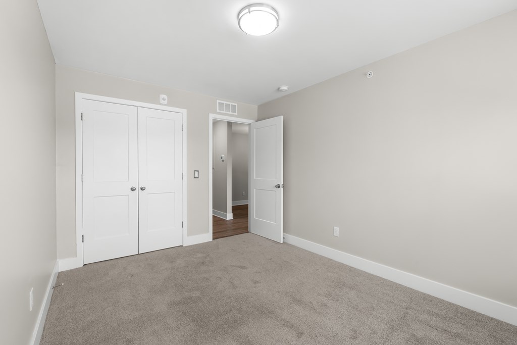 a bedroom with carpet and white doors and a door to a closet