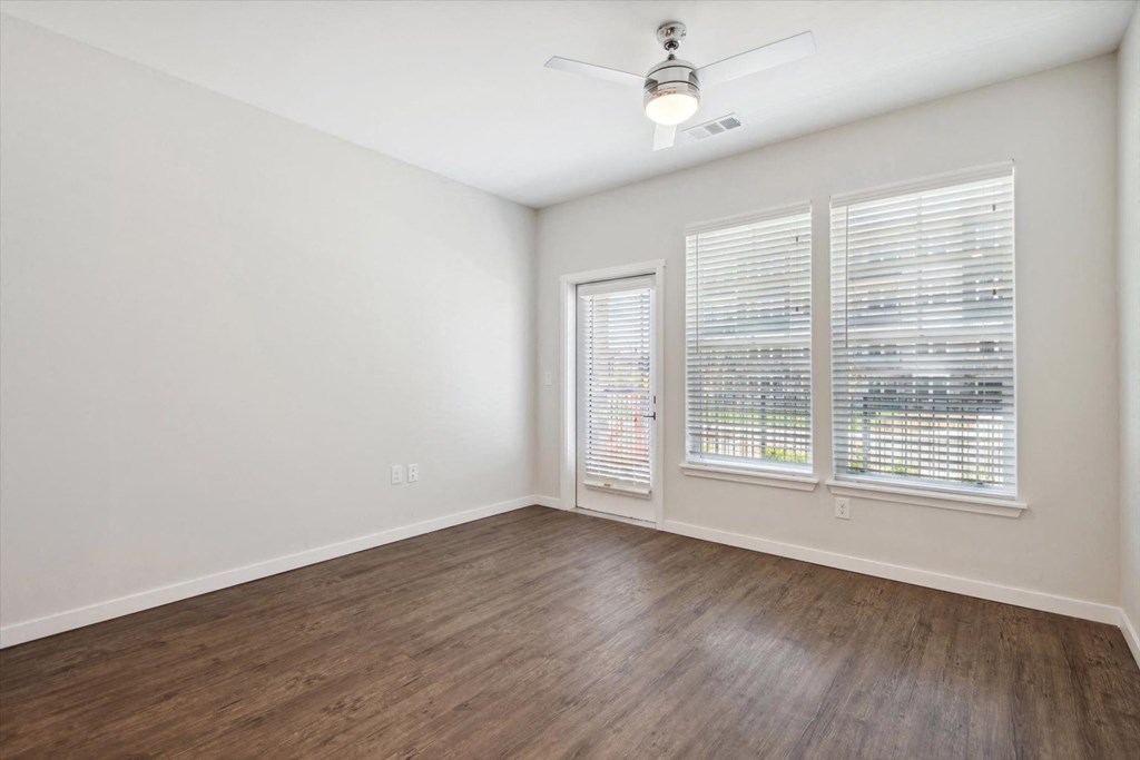 an empty living room with wood flooring and three windows