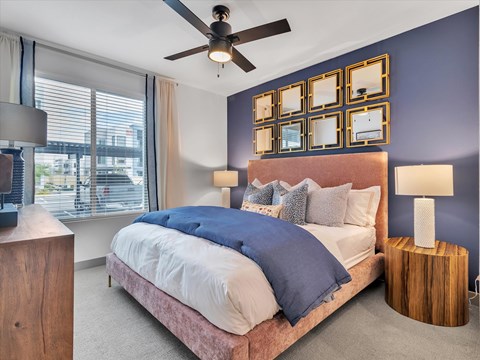 A bedroom with a bed, a ceiling fan, and a window with blinds.