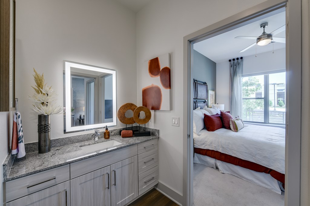 A bathroom with a large mirror and a bedroom in the background.