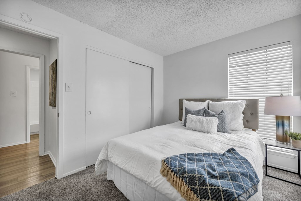 A bedroom with a bed, pillows, a blanket, a nightstand, and a lamp.