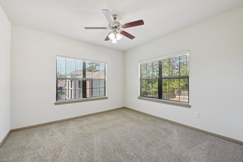 A room with a ceiling fan and two windows.